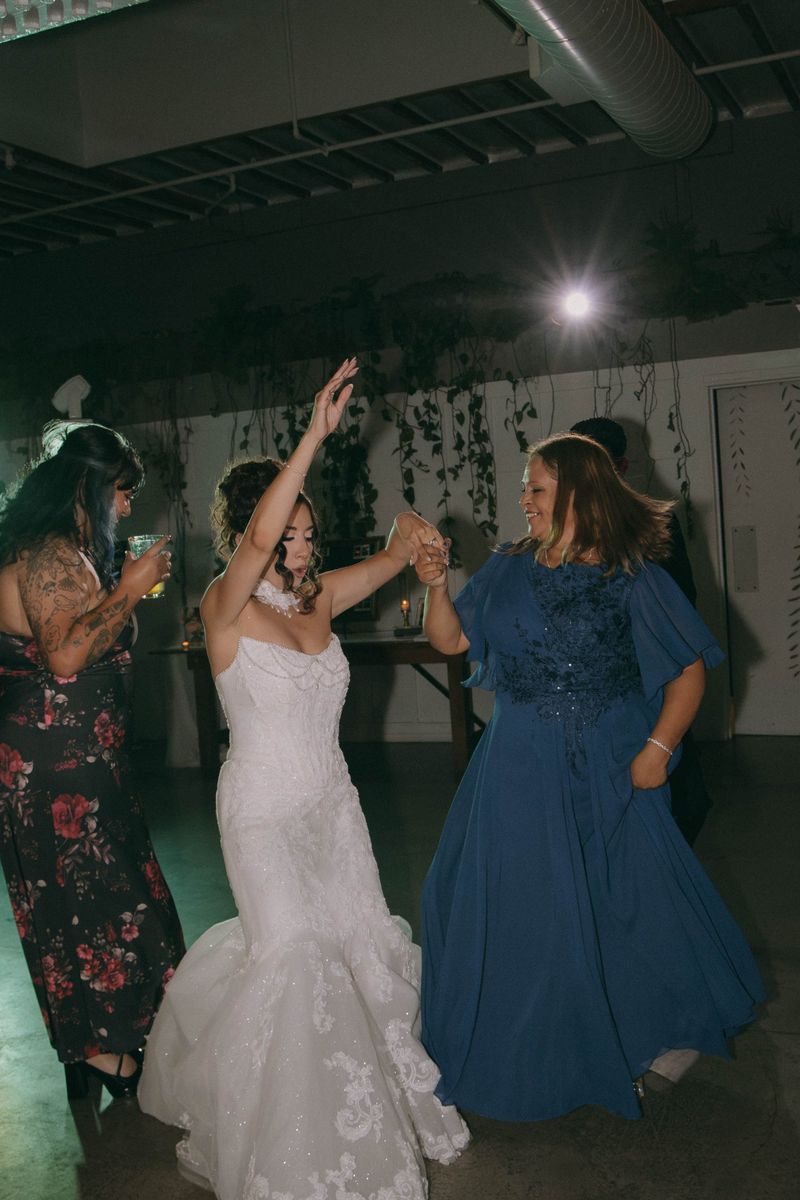 A bride dances hand in hand with an older woman in a blue dress