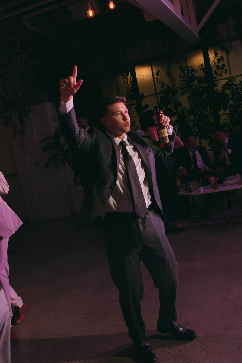 A guest in a suit dances with one hand pointing up under purple light